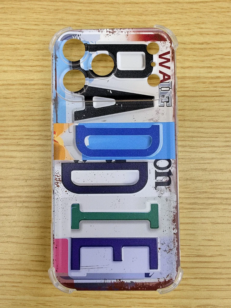 Finished transparent Baddie phone case on a wood table, showing distressed multicolor letters and the camera opening